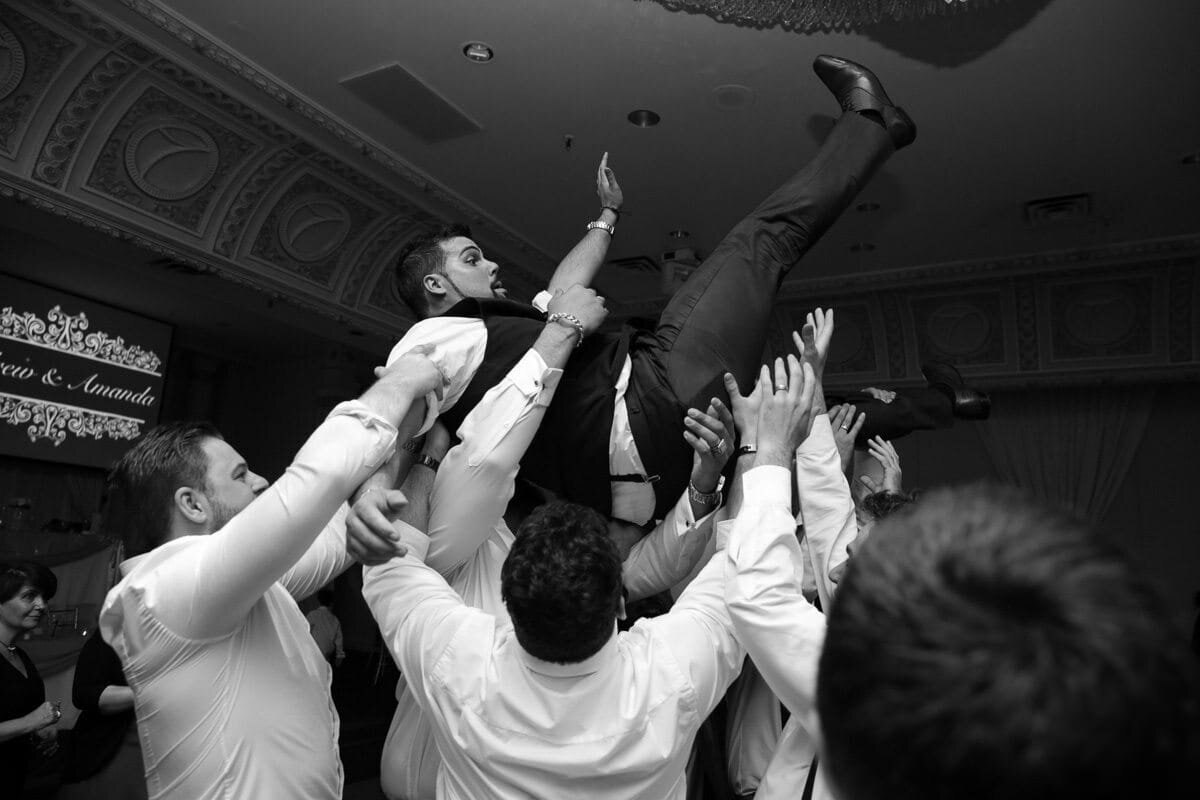 Groom lifted by friends during wedding reception celebration.