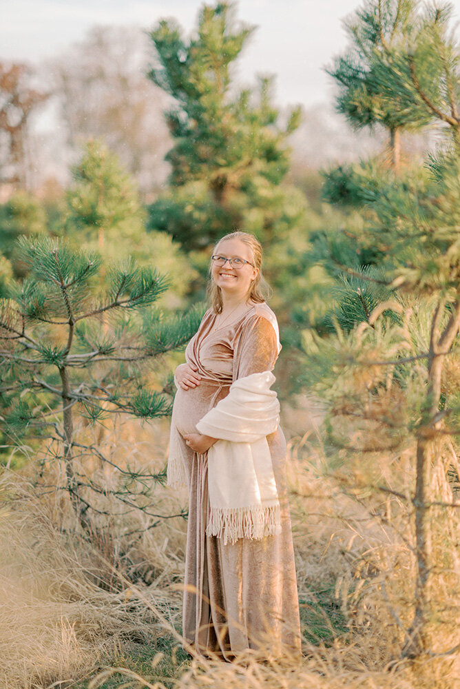 Woman in pink dress and white shawl for her Christmas maternity photos at a Chicago tree farm