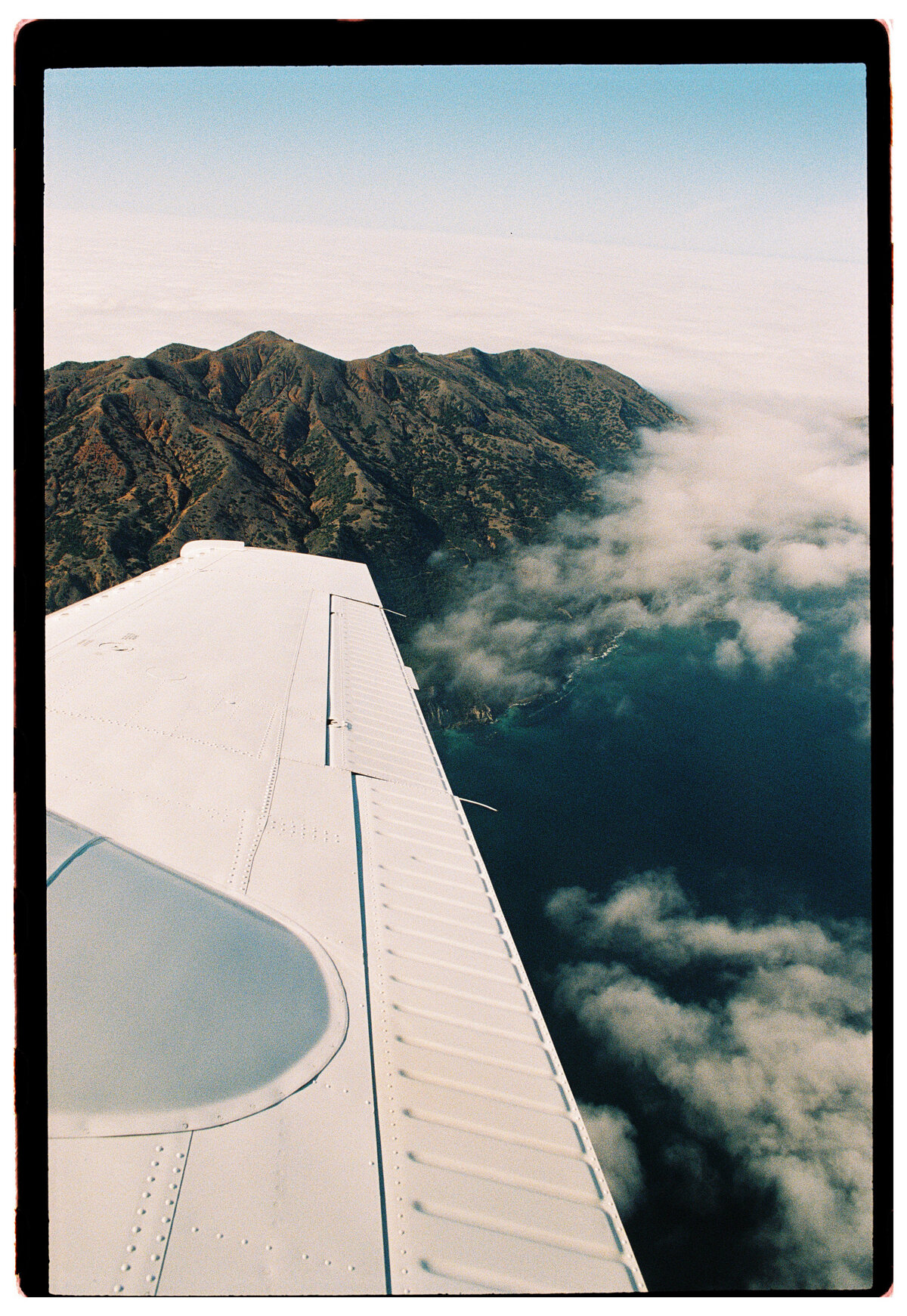 View of a plane wing overlooking the California coastline, captured by Kate Winters Photography in a candid, documentary style.