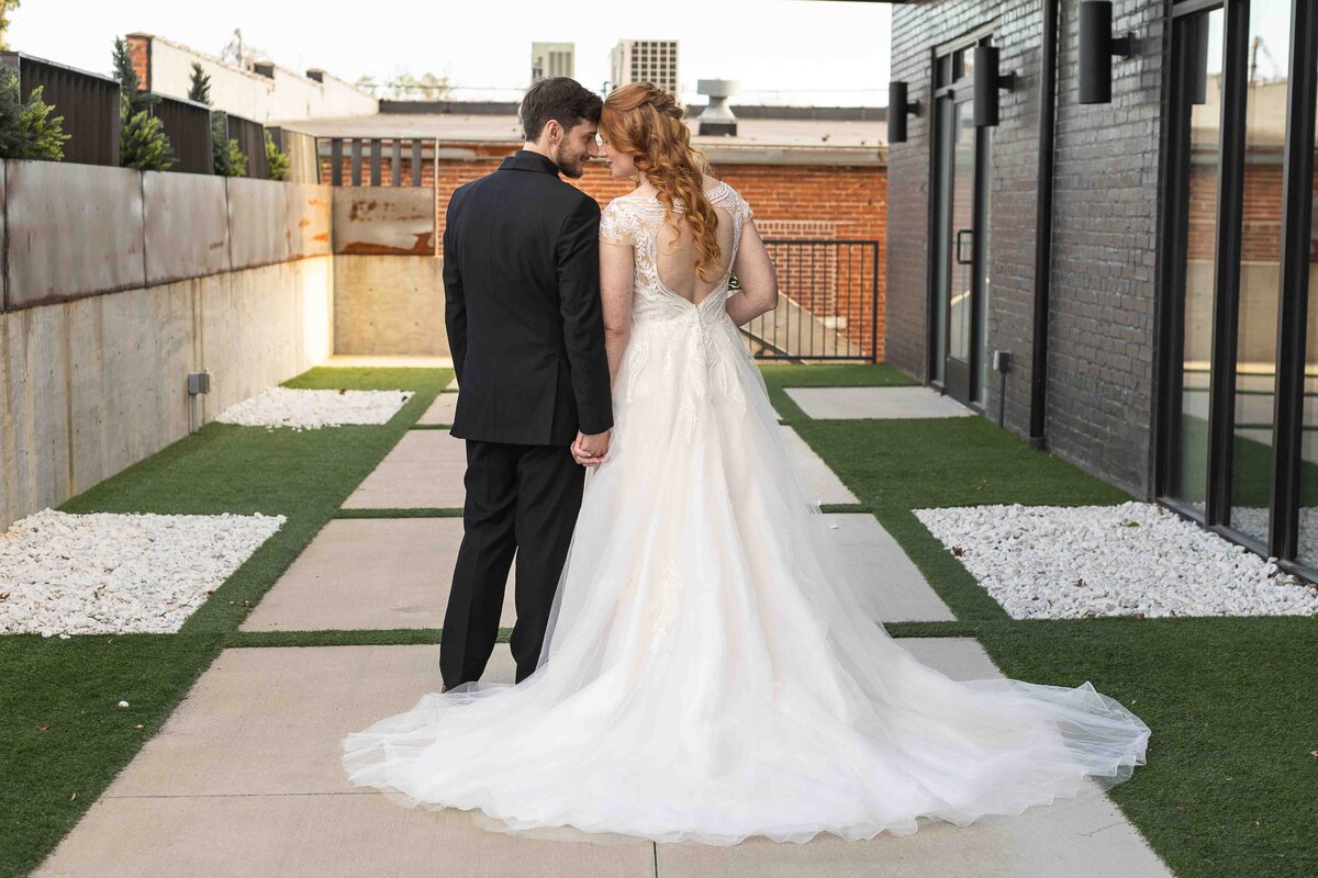 Bride and groom standing side by side holding hands and putting their heads together