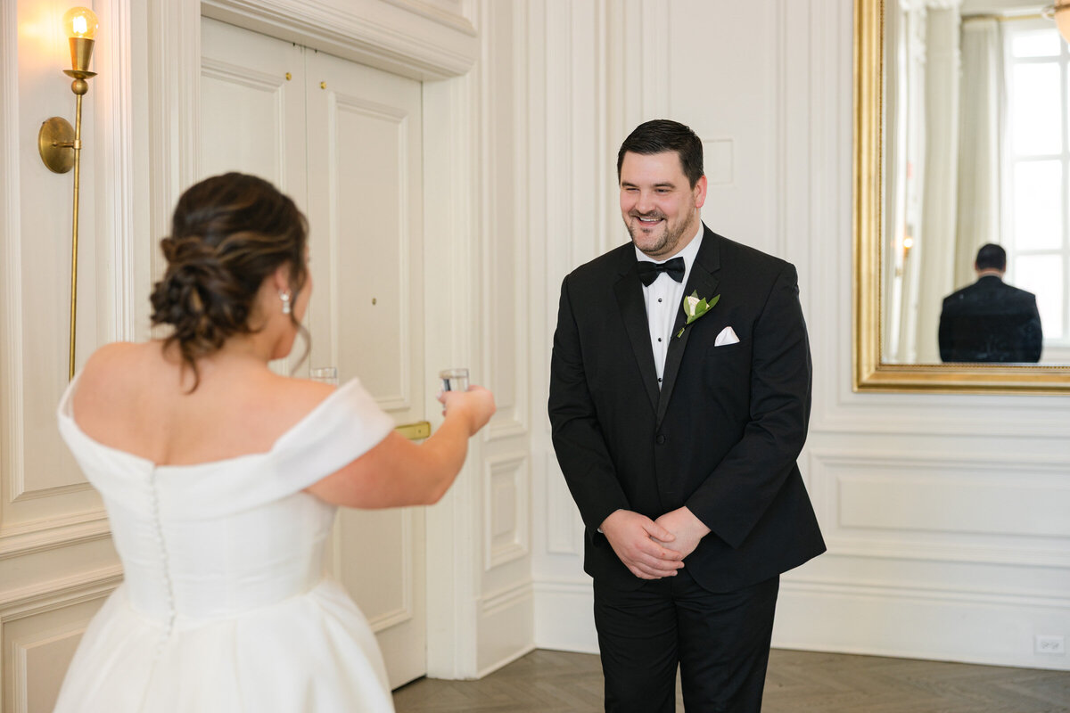 bride offering her groom a shot of tequila during their first look in the Governor’s Room at The Adolphus in Dallas, capturing a fun and candid wedding moment.
