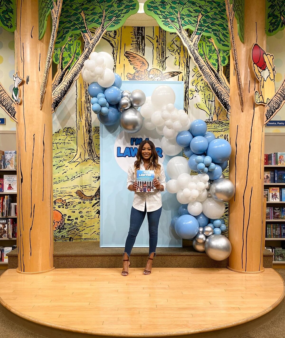 Woman posing in front of a blue, white a silver balloon arch backdrop at a book signing
