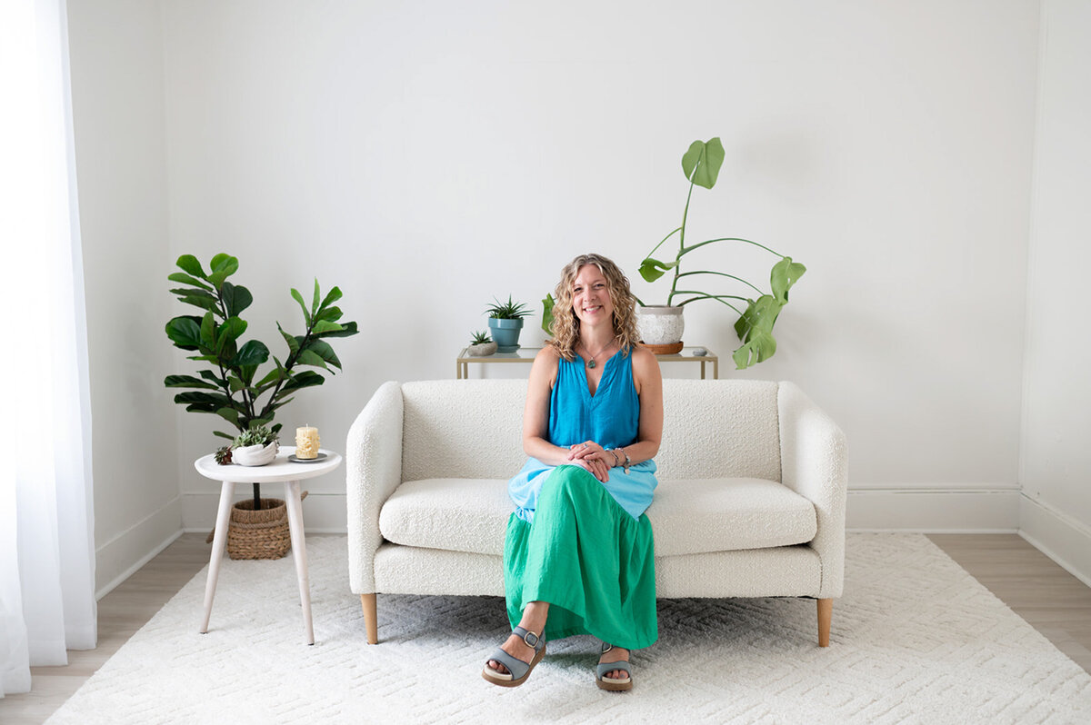 A woman named Heidi Schauster sitting on a white couch in a well-lit room.