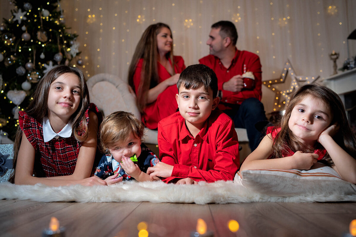 Family Christmas portrait in Calini Weddings Studio - children in festive outfits with parents smiling in warm holiday lights.