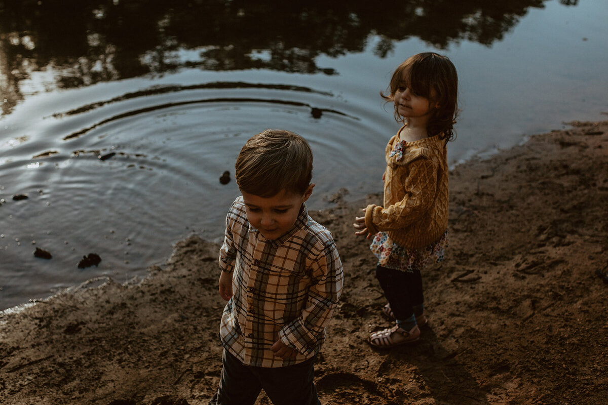 four year old twins throw stones in a lake 
