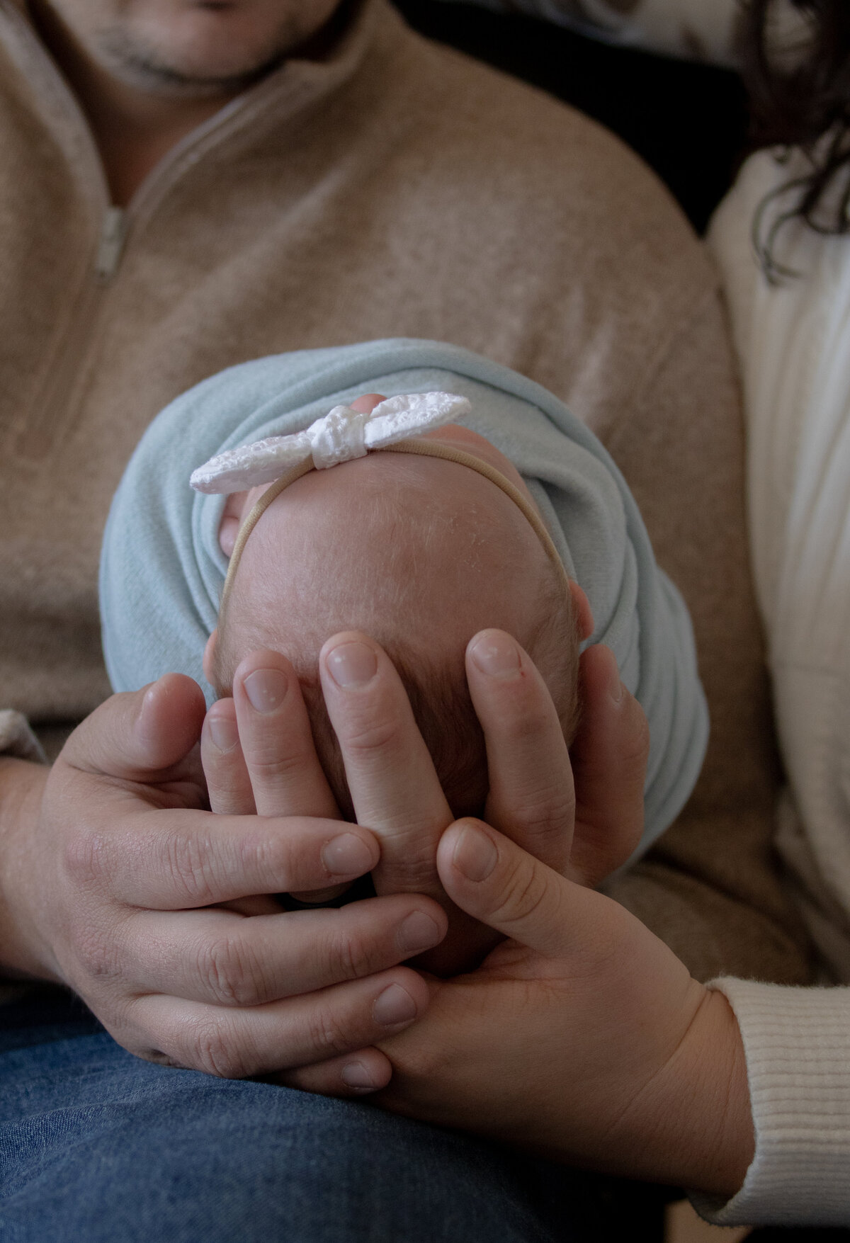 mom and dad caressing newborn baby's head while looking down lovingly at her swaddled on their lap