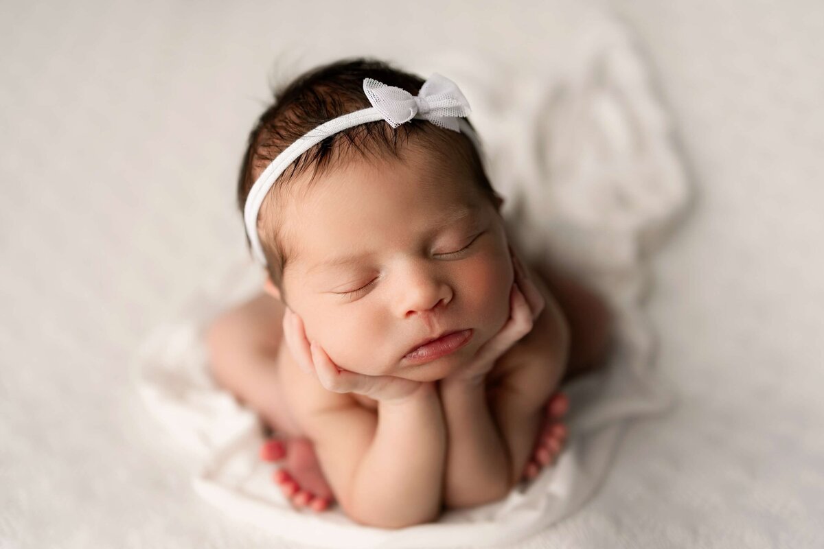 Denver newborn baby girl on a white blanket with her head in her hands