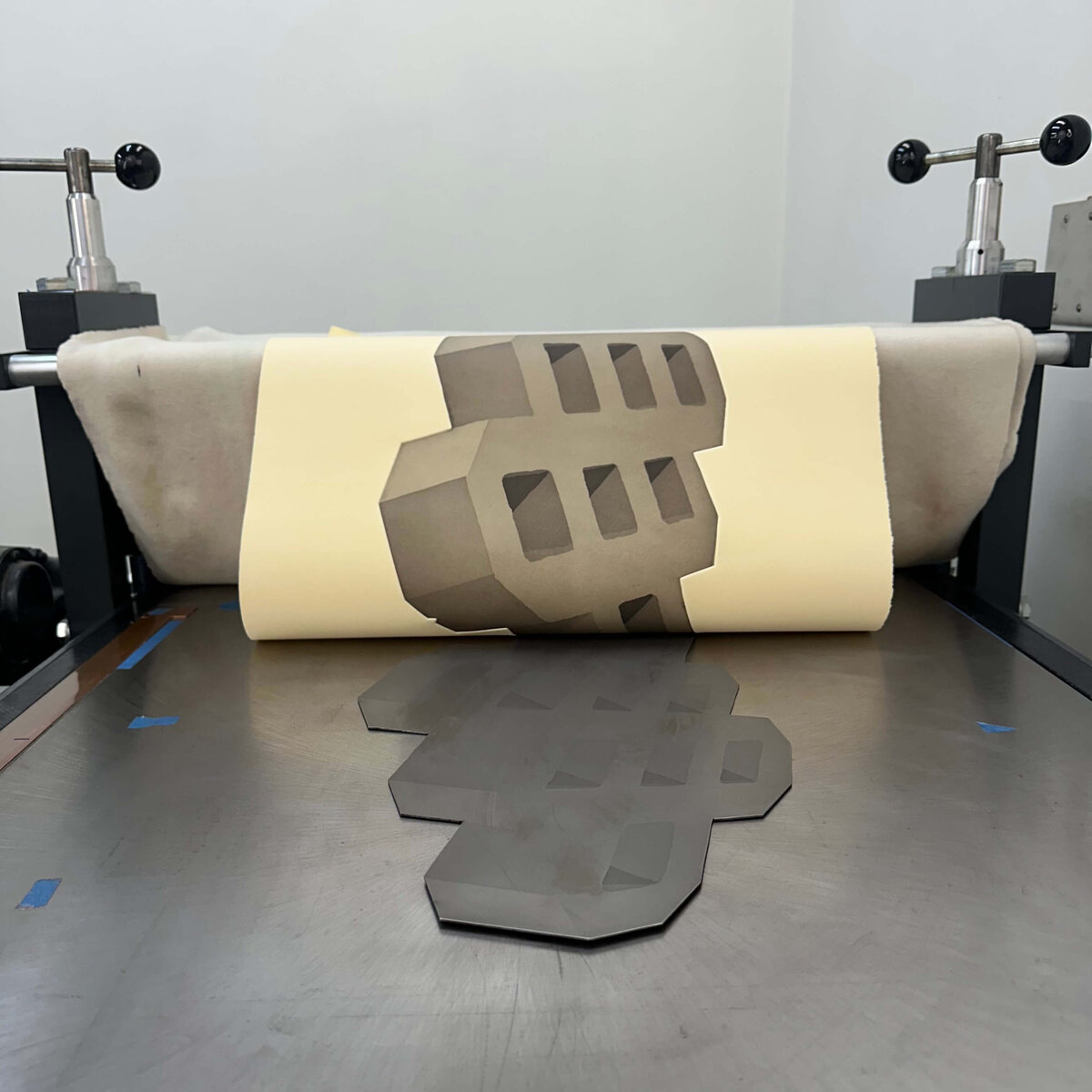 A freshly pulled aquatint print with geometric depth sits half-rolled on the etching press bed, the plate still visible beneath.