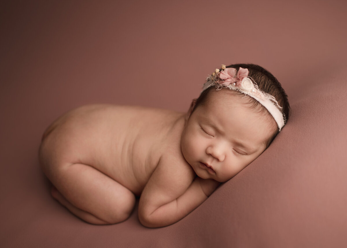 Newborn baby girl is posed bare for her Lake Elsinore newborn photoshoot. She is sleeping on her belly with her legs curled underneath her.