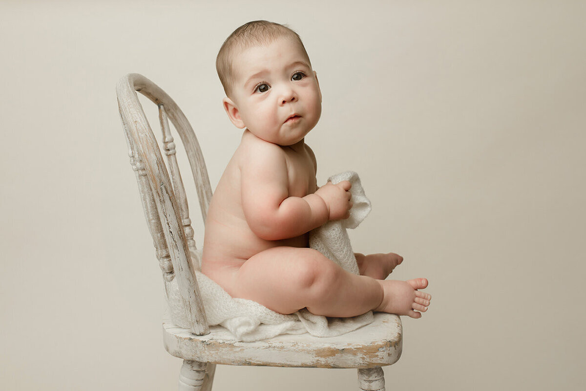 a six month old baby pouting in a white chair and a white wrap