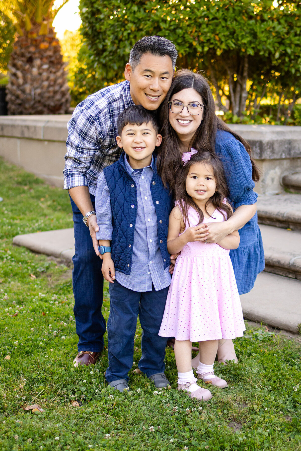 Bay Area Family Portfolio - Ellobelle Photography shows a cheerful family of four posing together on green grass, smiling warmly with lush greenery in the background.