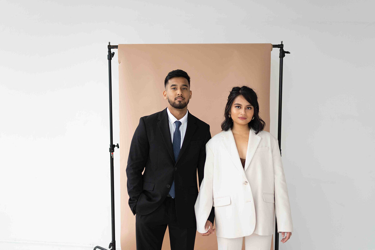 Couple facing camera holding hands in front of tan studio backdrop