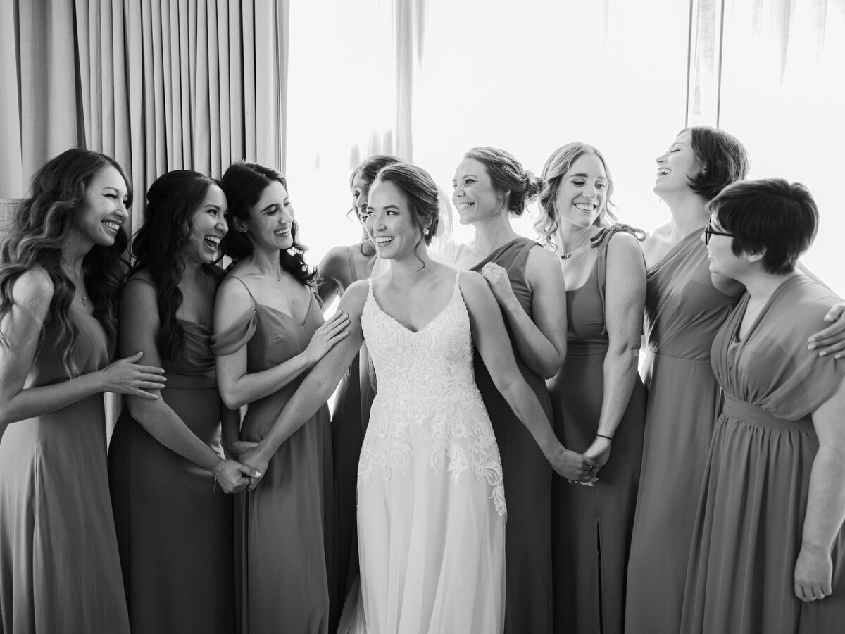 A bride holds the hands of her bridesmaids as they all laugh with each other