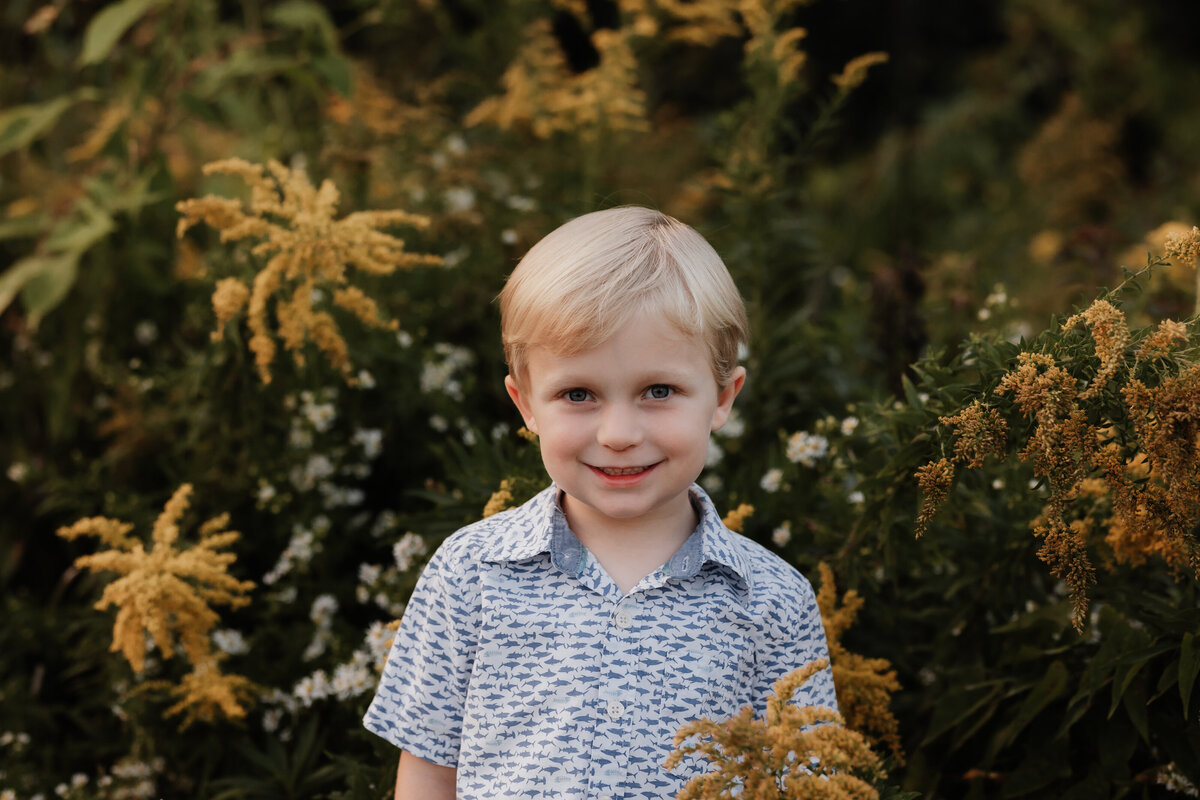 A boy smiles for the camera in yellow flowers.