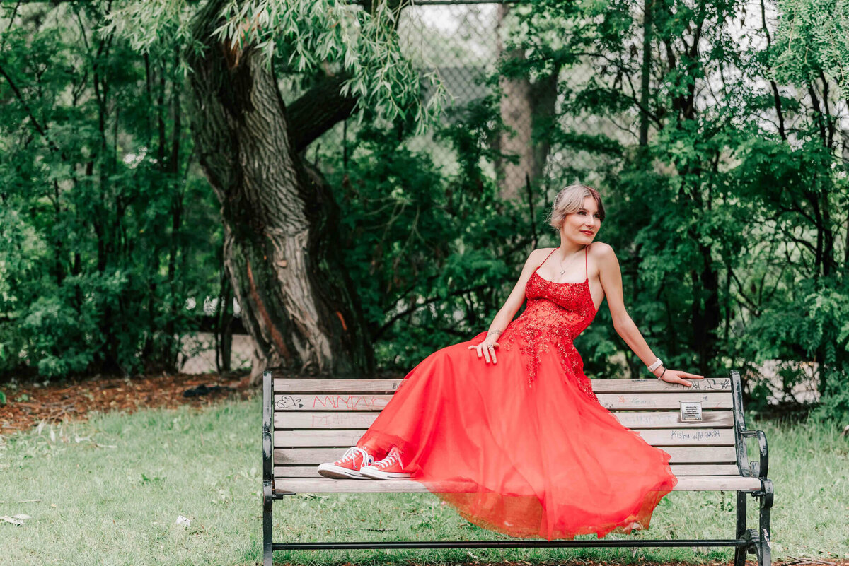 A full length image of a girl sitting on the top of a bench. 