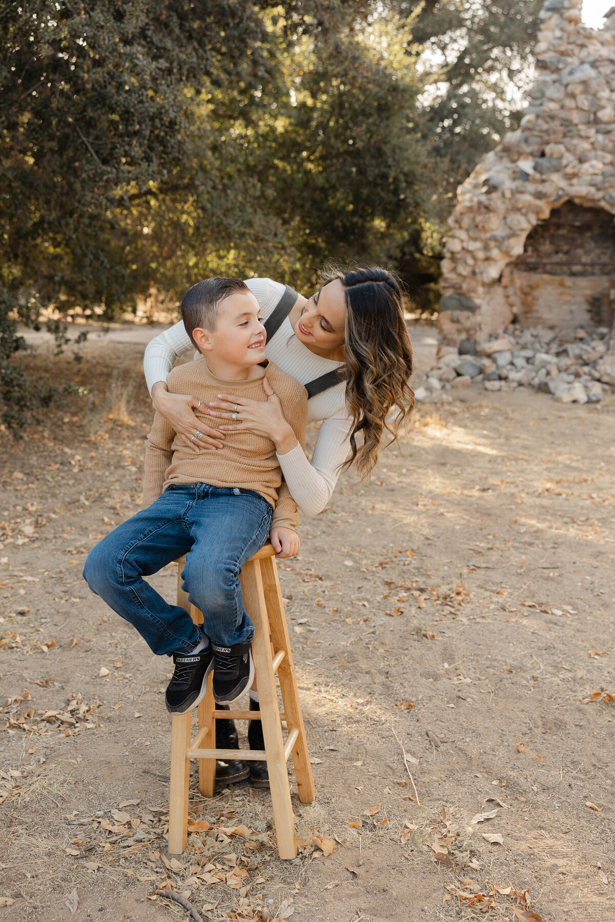 Boy sitting on chair outdoors in neutral sweater and jeans, smiling at camera. Photographed by Yucaipa family photographer Kaitlyn Dawn Photography.