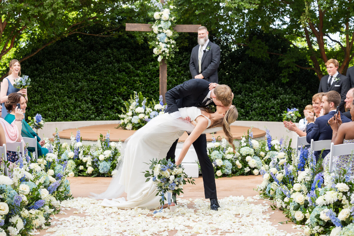 Spring wedding at WinMock at Kinderton, designed by Charming Carolina — bride and groom pause for a kiss halfway down the flower-lined ceremony aisle.