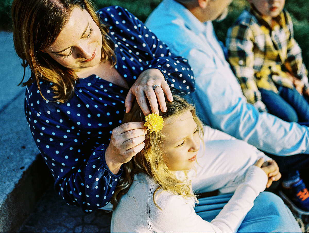 mom puts flower in daughter's hair while sitting on steps at park