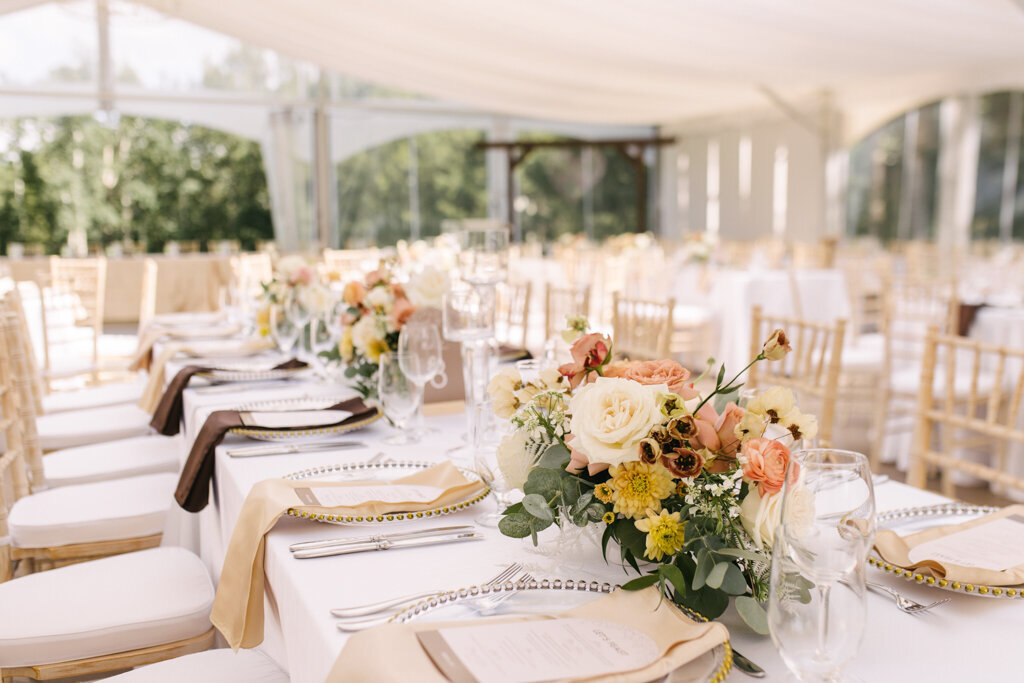 White tented wedding reception with white, yellow, pink, and burgundy Fall inspired florals designed by More Events Co, featured on the Brontë Bride Vendor Guide.