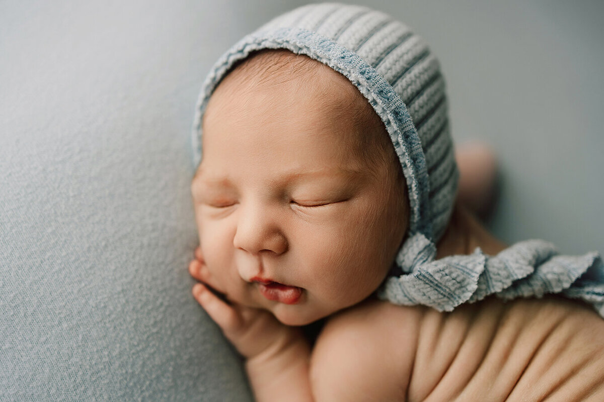 Side view of baby boy in a blue bonnet with his back rolls showing