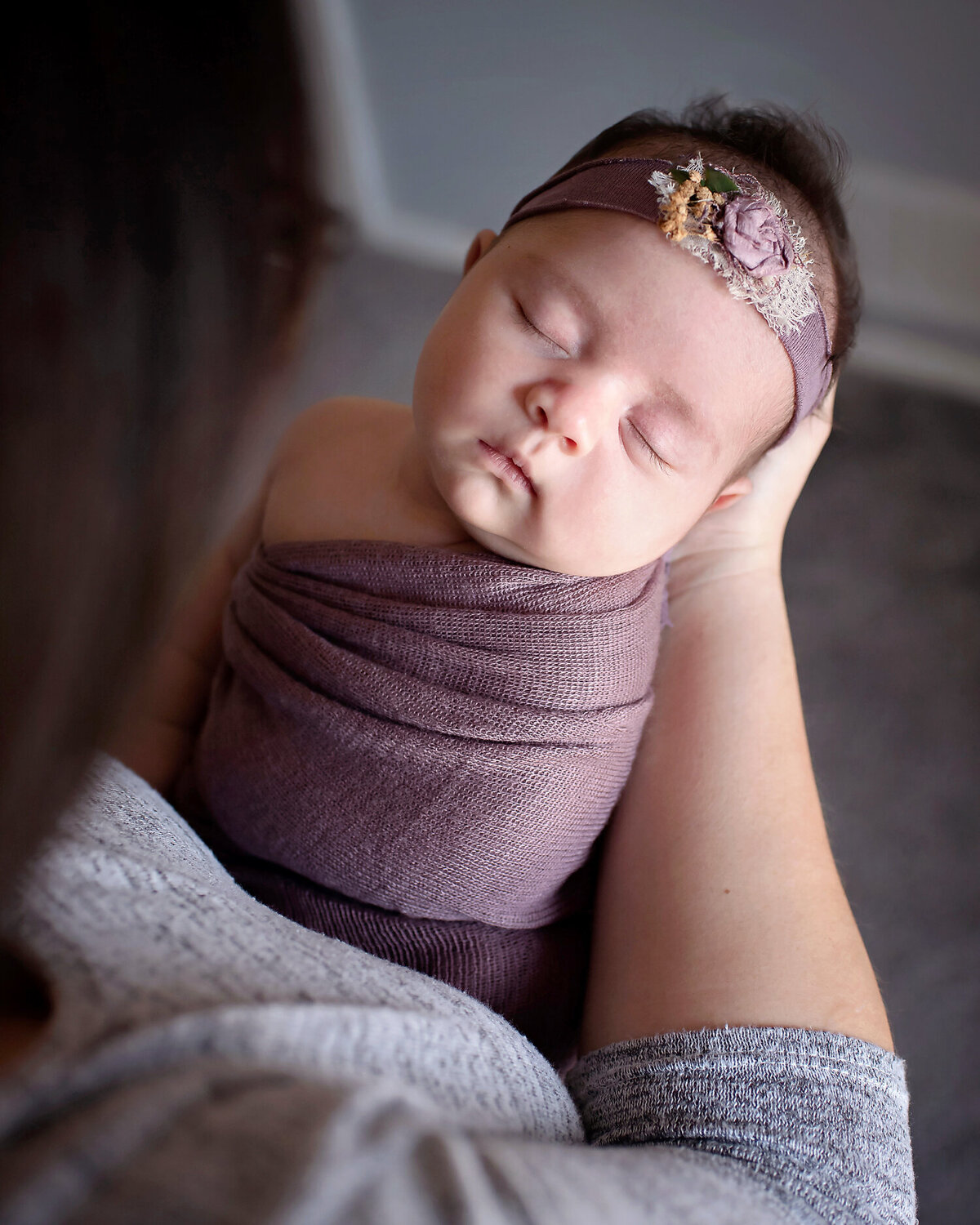 Beautiful newborn girl in a purple wrap and matching headband, sleeping in her mother's arms.