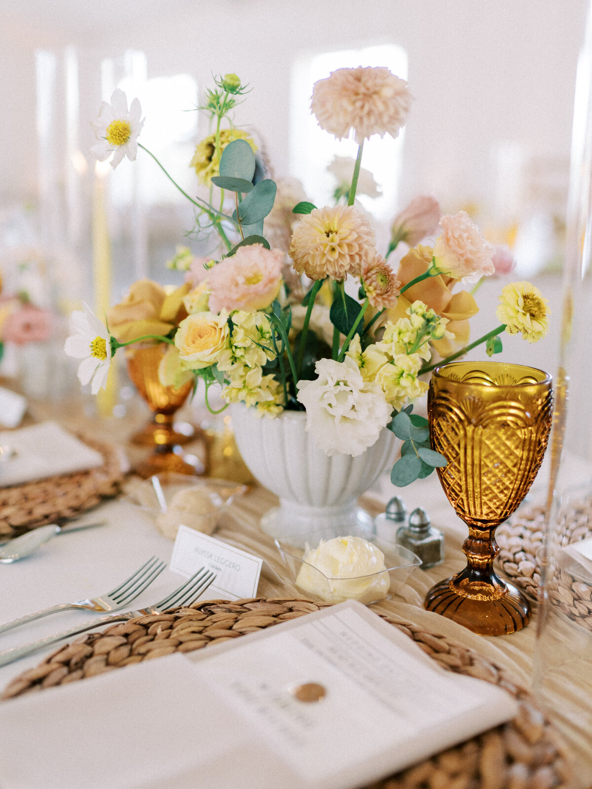 wedding tablescape with peach and yellow tone floral arrangement, a mustard toned crystal glass, candles and menus tucked in taupe napkins taken by Mansfield Wedding Photographer, Annie Trammel