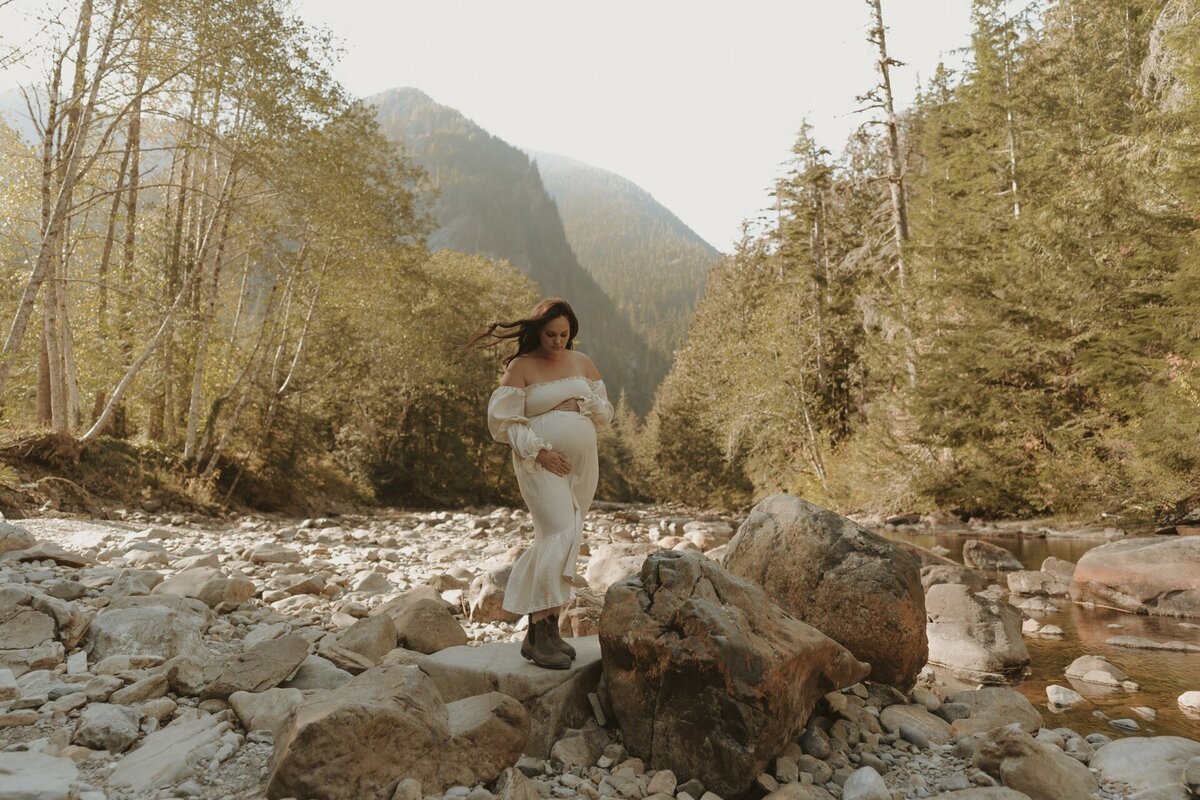 pregnant female wearing cream dress standing on rock at california creek