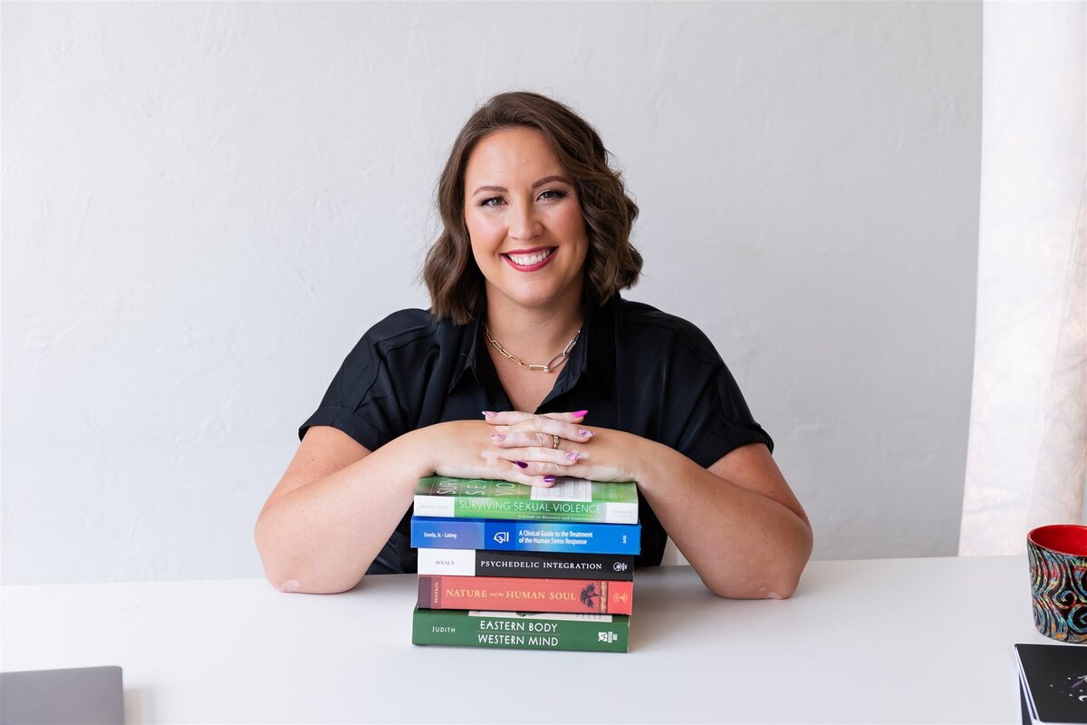 Women's empowerment speaker, Kathryn Konicek, sitting behind a desk with a stack of books