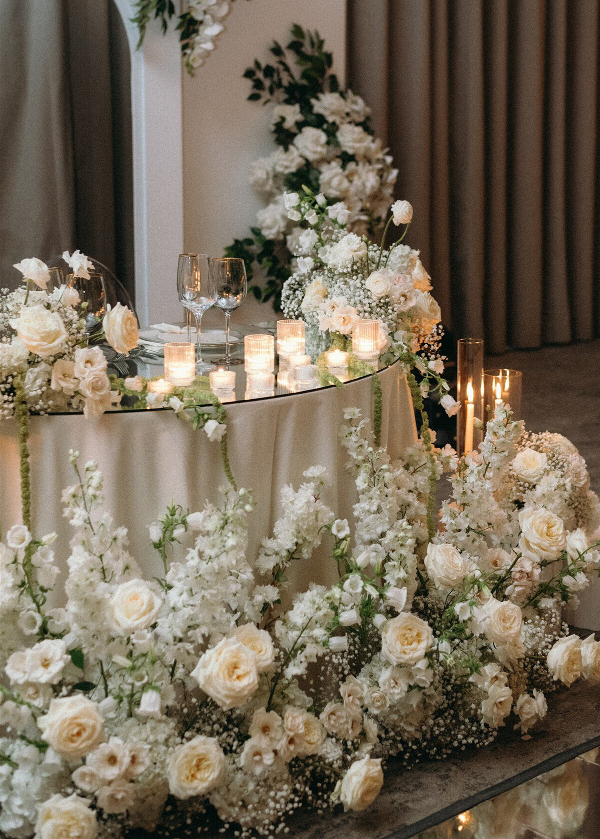 A sweetheart table for a wedding at Westbury Ballroom is framed by a meadow of elegant, lush white flowers.
