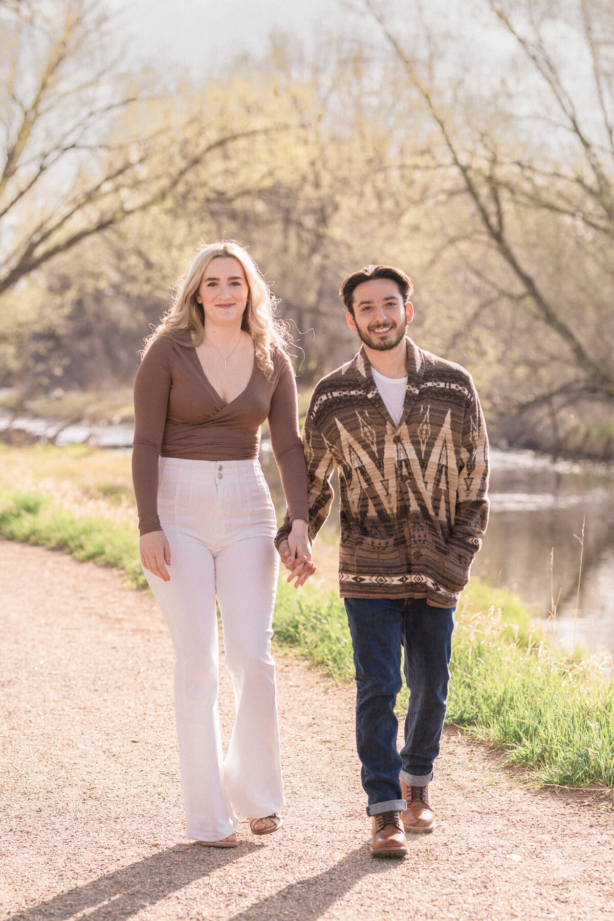A casually dressed engaged couple walk toward the camera on a footpath beside Boulder Creek