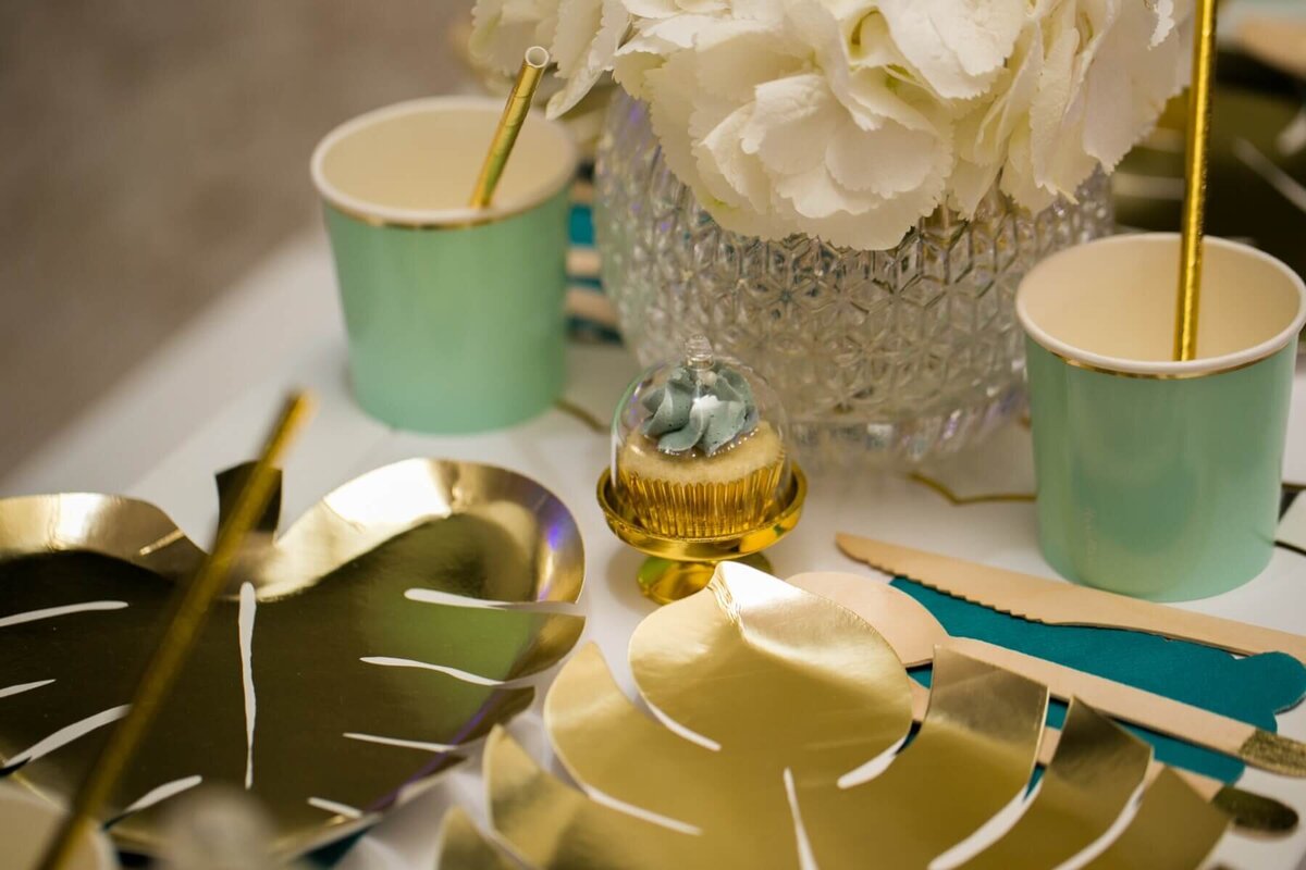 Mini cup cake on a gold cake stand with turquoise cups and gold straws