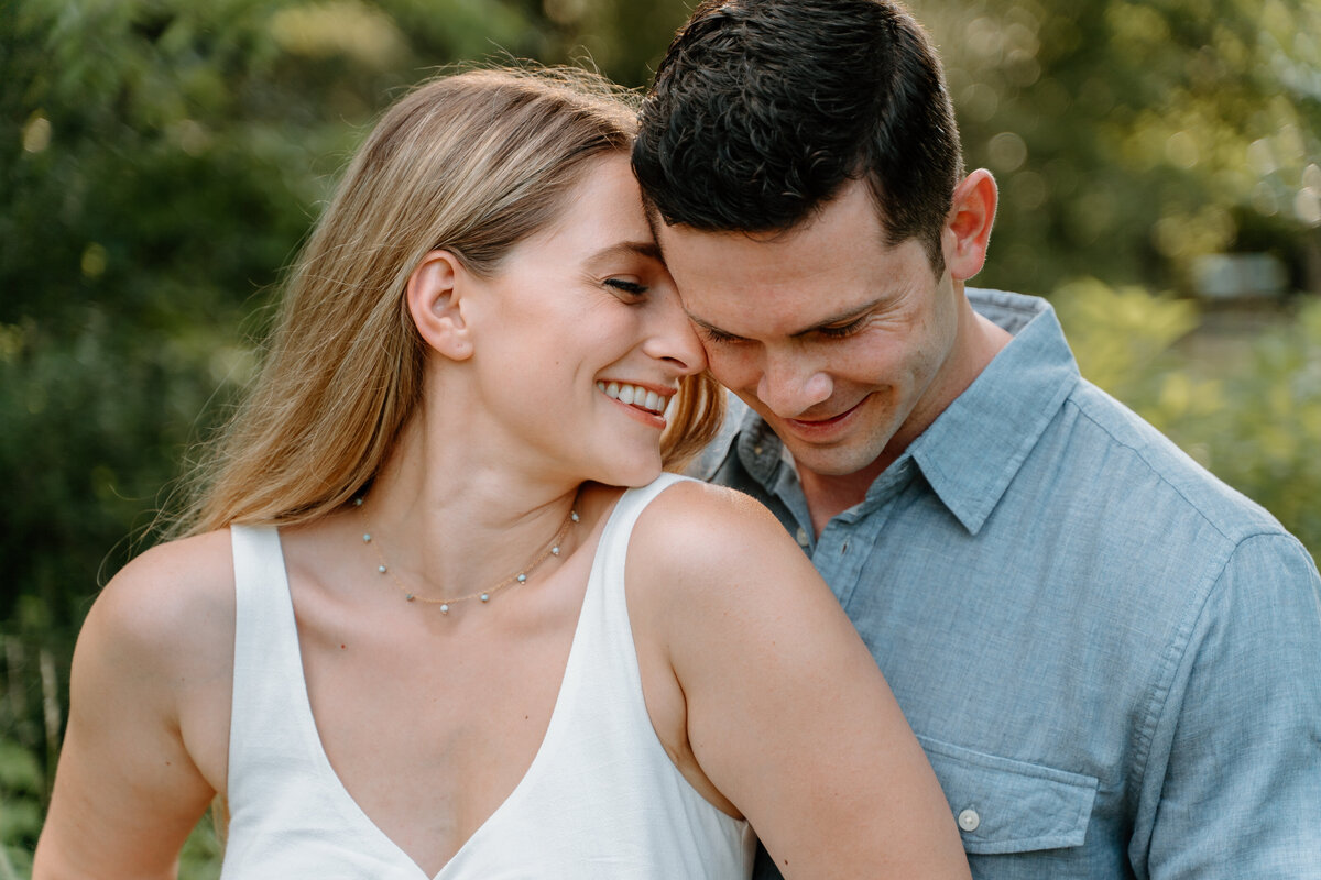 Outdoor springtime engagement photos of couple embracing with greenery surrounding.