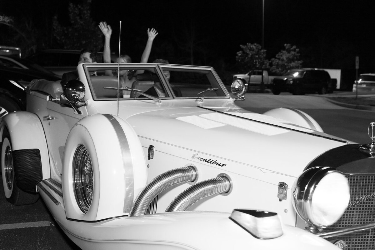 Bride and groom raise their hands from a vintage white Excalibur convertible during their Burritt on the Mountain wedding exit.