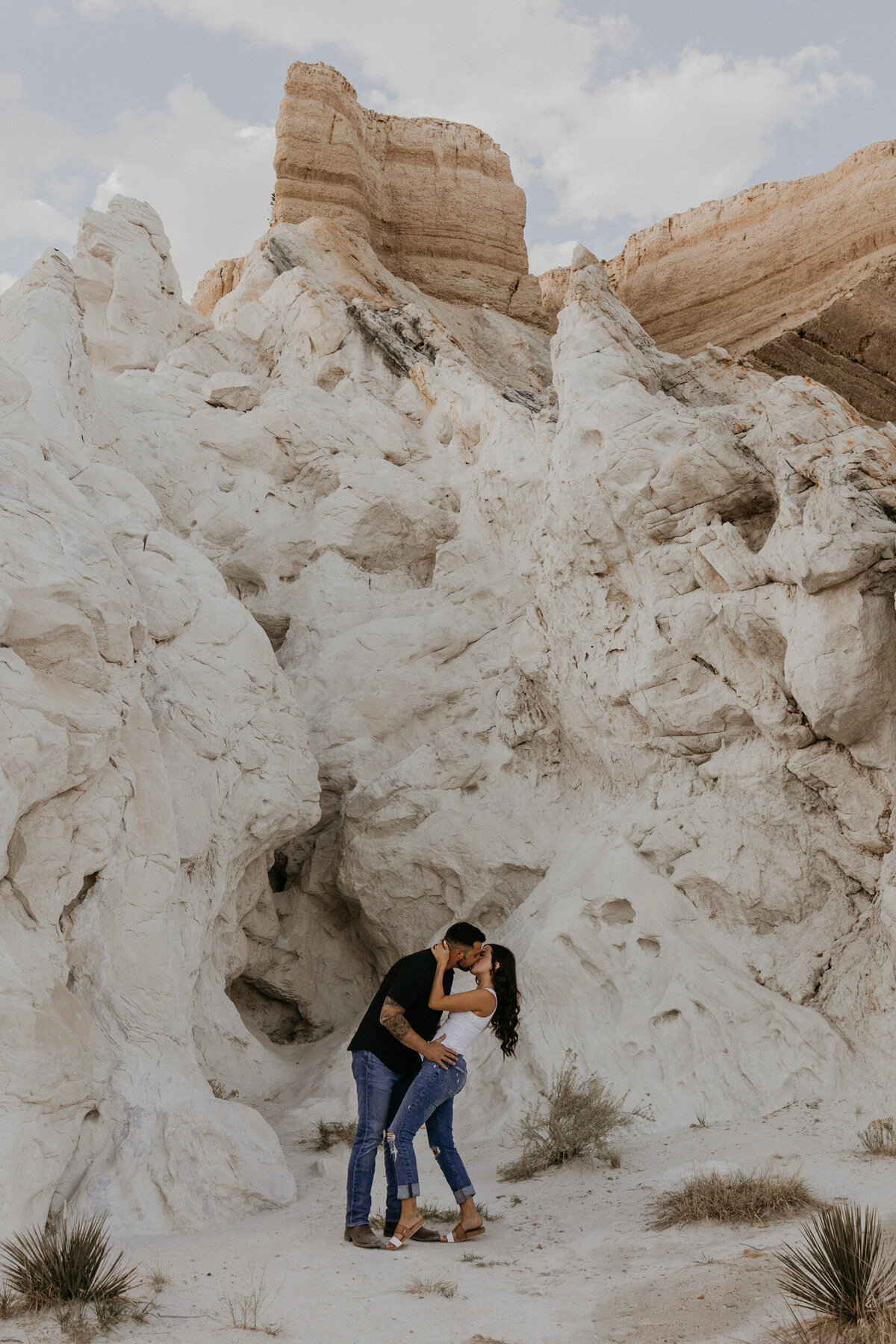 engaged couple kissing in front of a white rock in the desert
