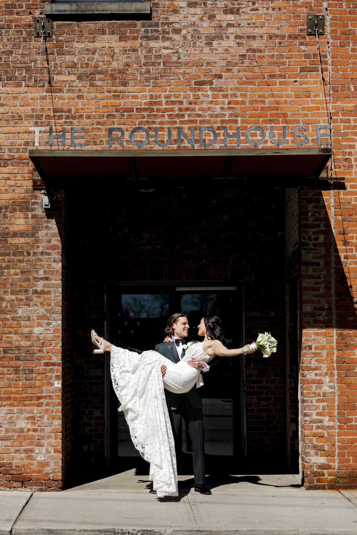 The groom picks up the bride under the Roundhouse hotel sign in Beacon