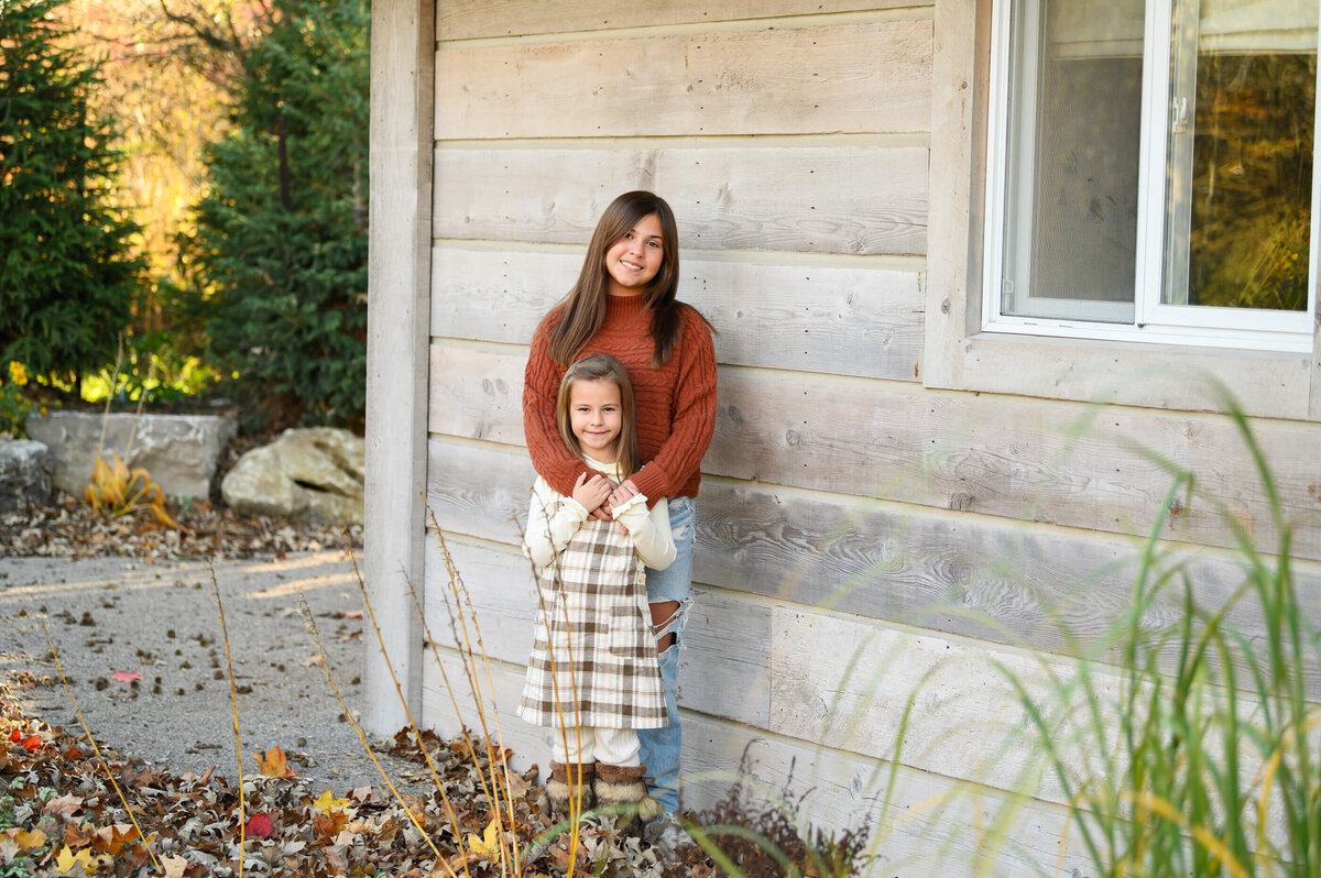 sisters standing against a cabin for their fall family photos in Burlington, On