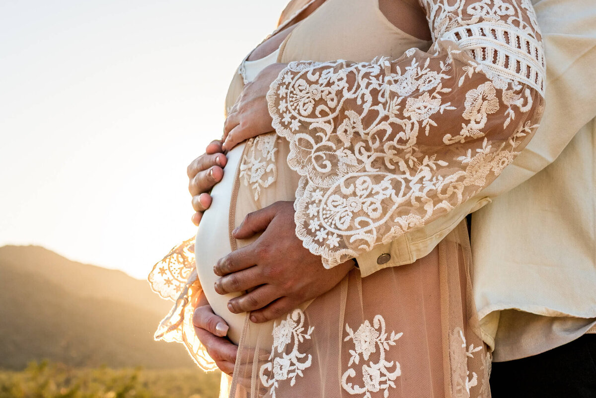Maternity belly cradled by parents during Arizona sunset. Captured by Cactus & Pine Photography