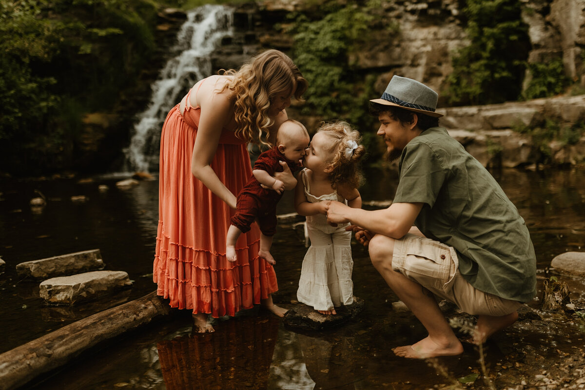 sister kisses sibling while parents pose for photo