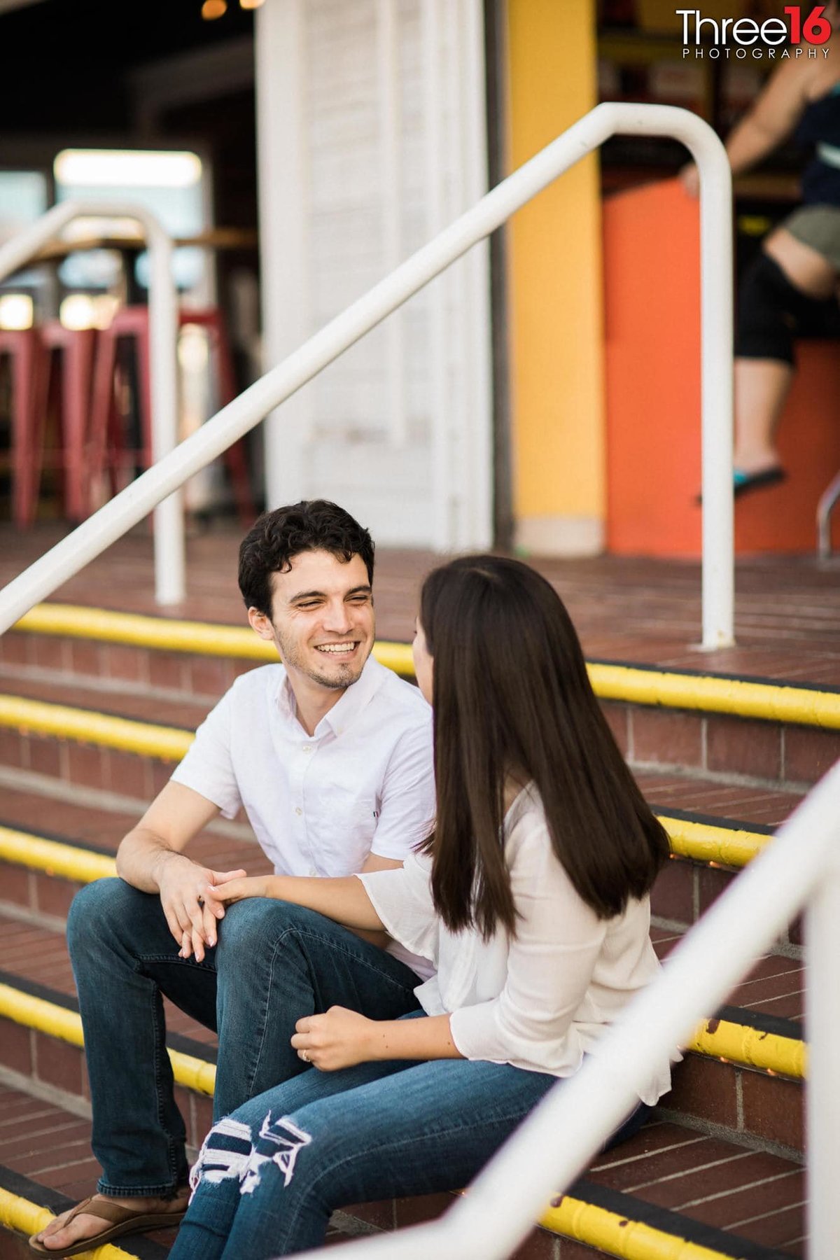 Couple smiling at each other while sitting on arcade steps