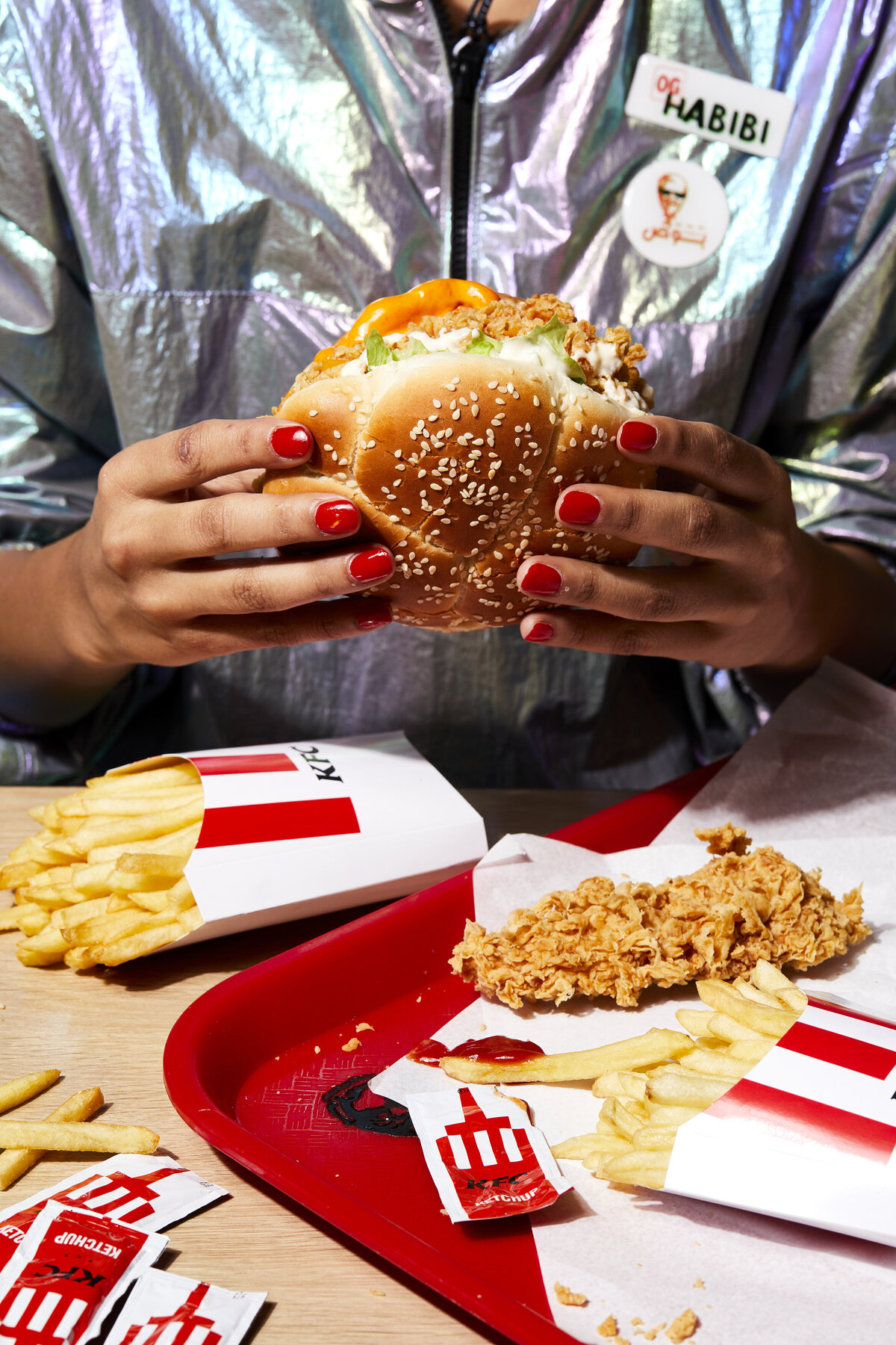 Hands holding a chicken sandwich over a tray of fries and ketchup packages.