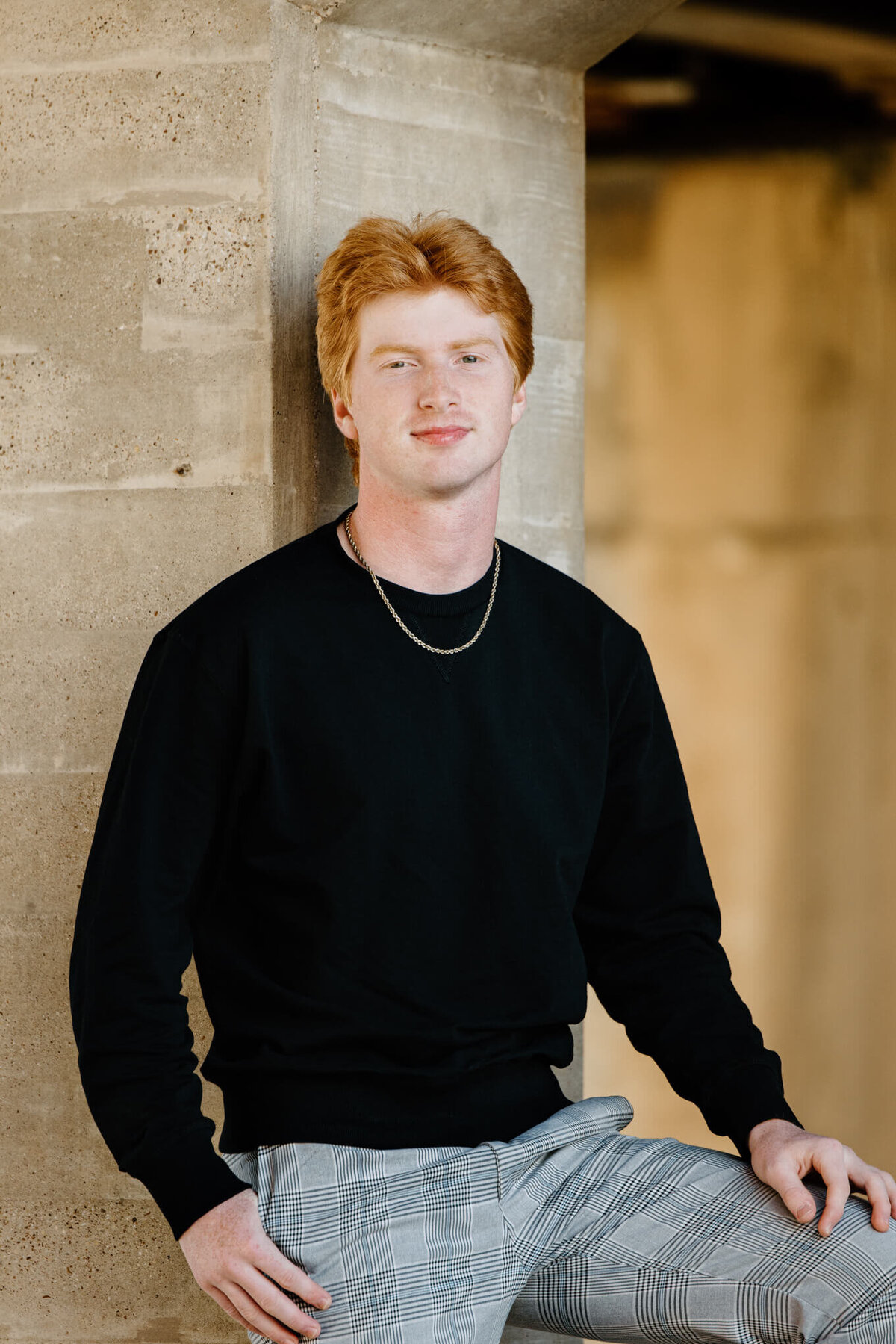 Senior photo of graduate in black sweater leaning on concrete wall in downtown Longview, TX