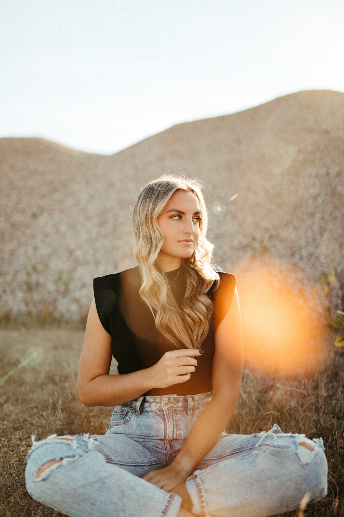 Senior with blonde hair sitting Indian style and playing with her hair