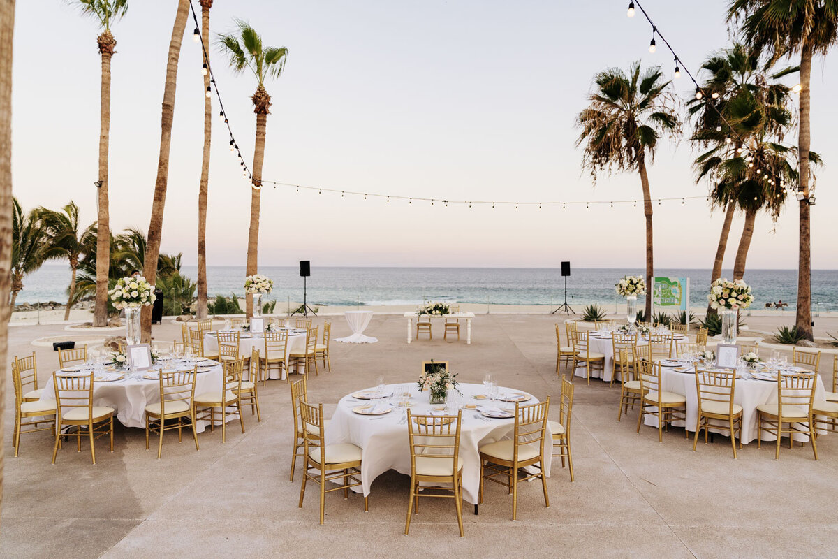 Elegant outdoor reception setup with tables and palm trees by the beach