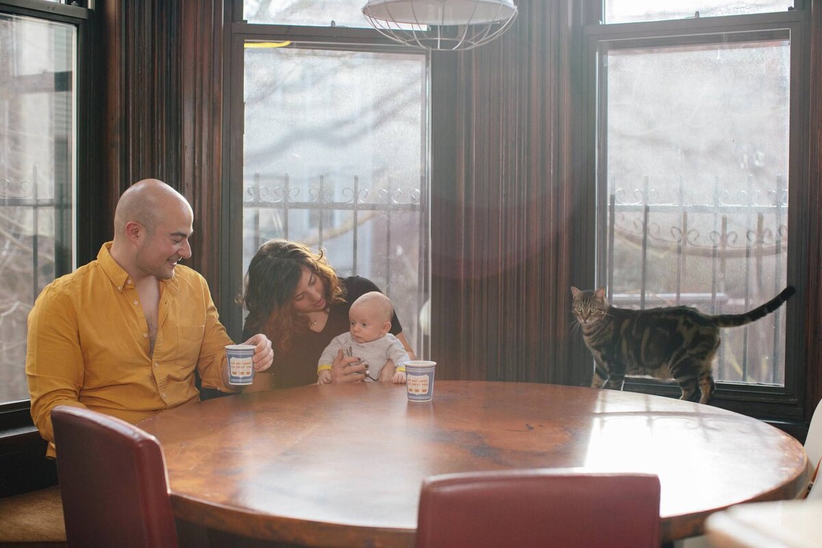 brooklyn family photo of a couple with coffee baby and cat at the kitchen table
