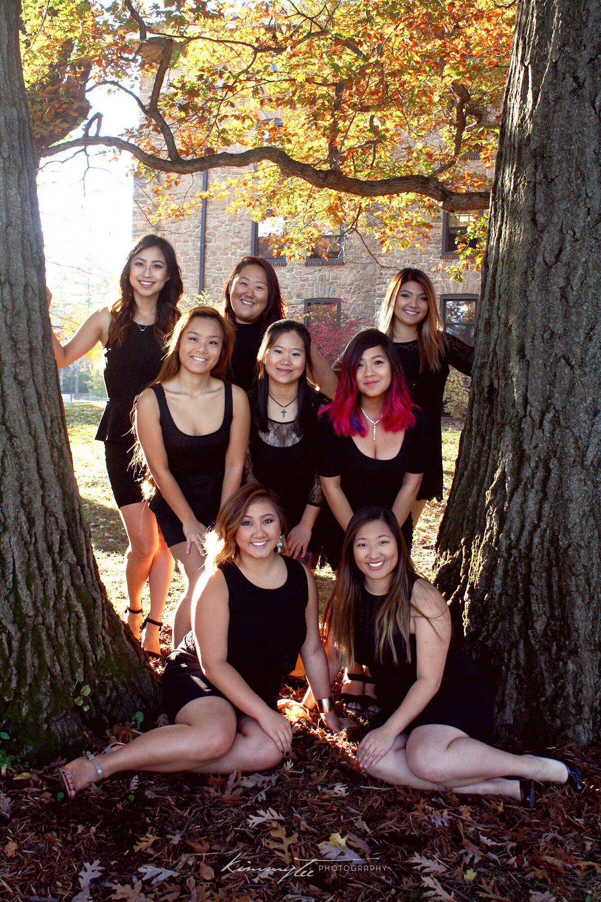 Eight sorority girls on a fall day posing between two trees with autumn leaves