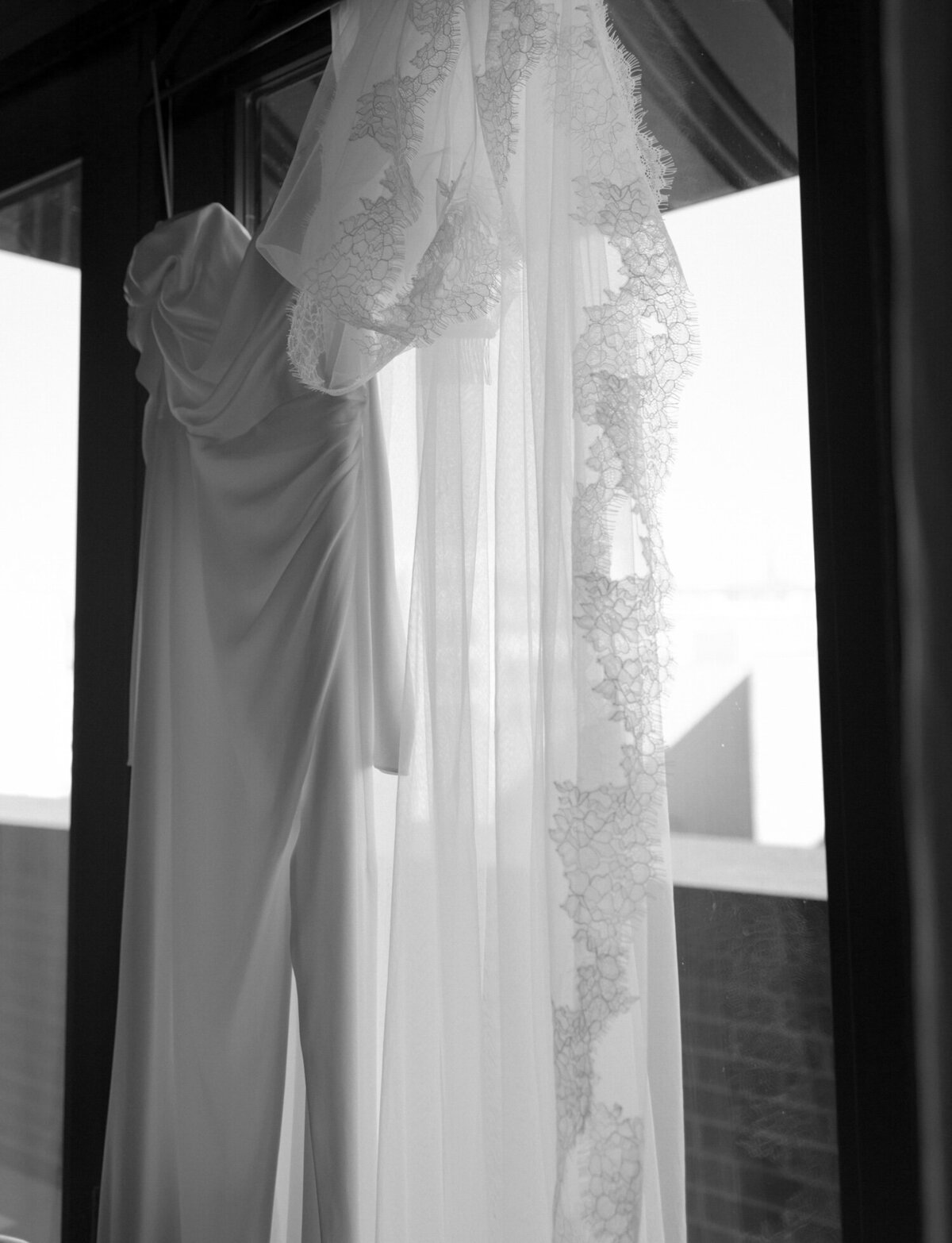 Lace detail on a long cathedral veil and silky wedding dress hang at Shinola Hotel