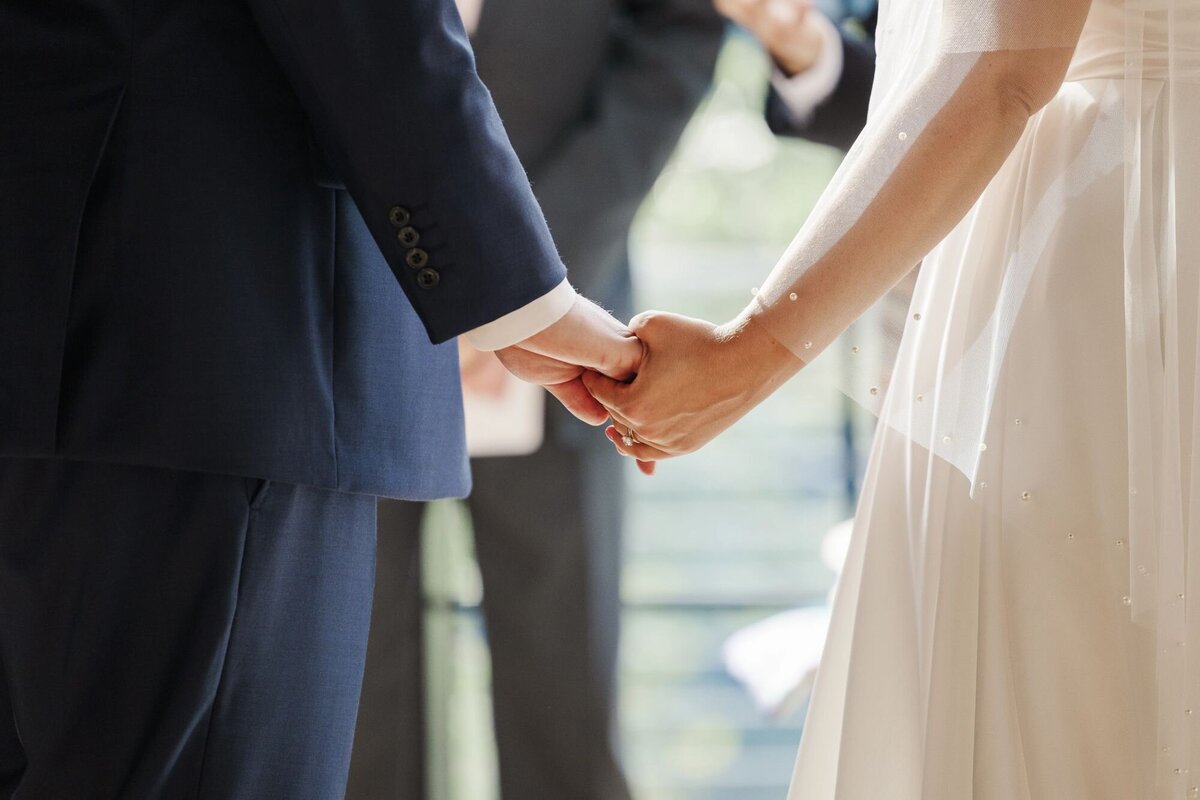Up close photo of bride and groom holding hands during indoor ceremony at The Roundhouse