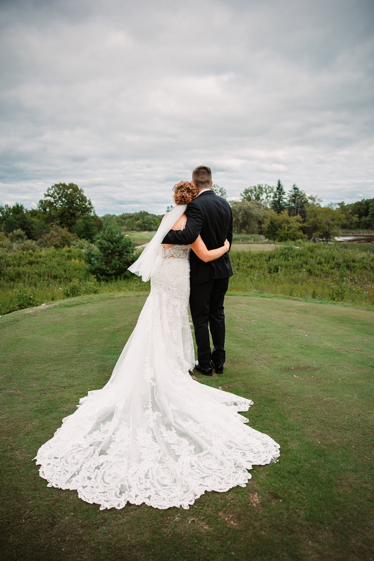 A bride hugs her groom with her lace train extended behind her on a golf tee