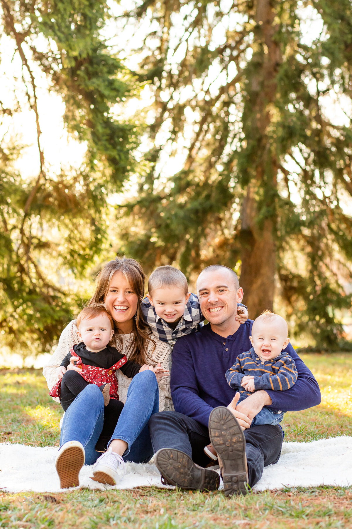 Family sitting on blanket giggling into the camera with pine tree backdrop