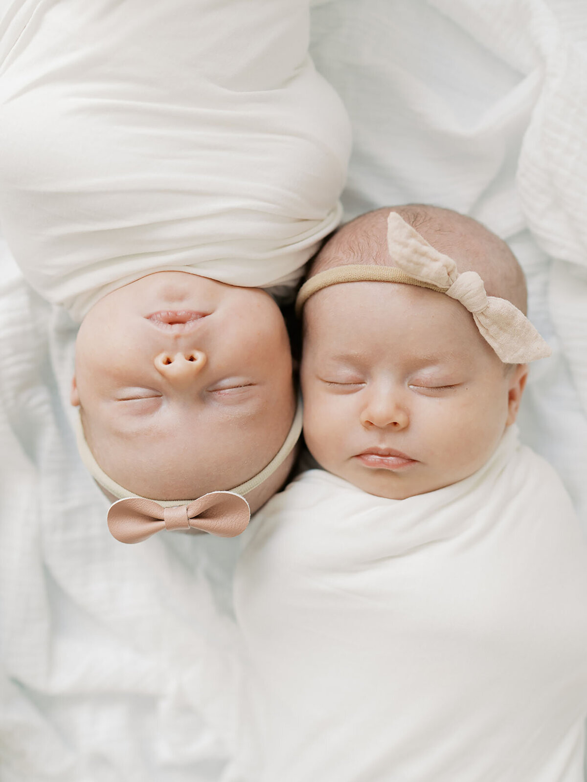 Newborn twin girls are swaddled and lying side by side in a basket, peacefully resting together. Their tiny features and close bond are captured in this sweet and serene moment.